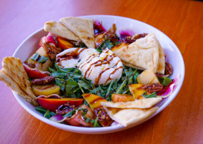 Peach & Burrata Salad A salad with a huge piece of Burrata in the center surrounded by colorful peaches, heirloom tomatoes, candied pecans, watermelon radish.